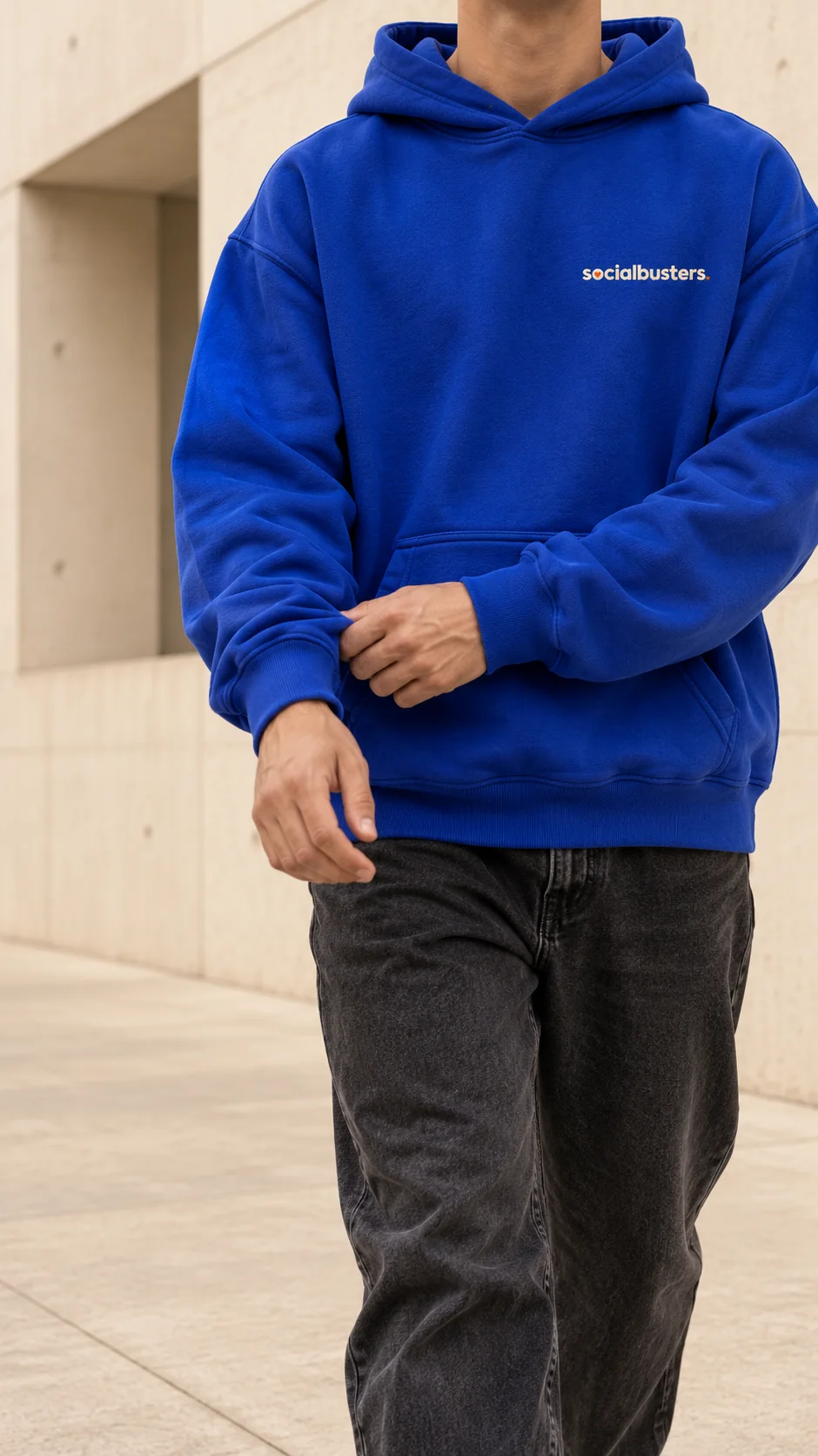 Iemand in een blauwe hoodie met het Socialbusters-logo op de borst, lopend langs een betonnen muur